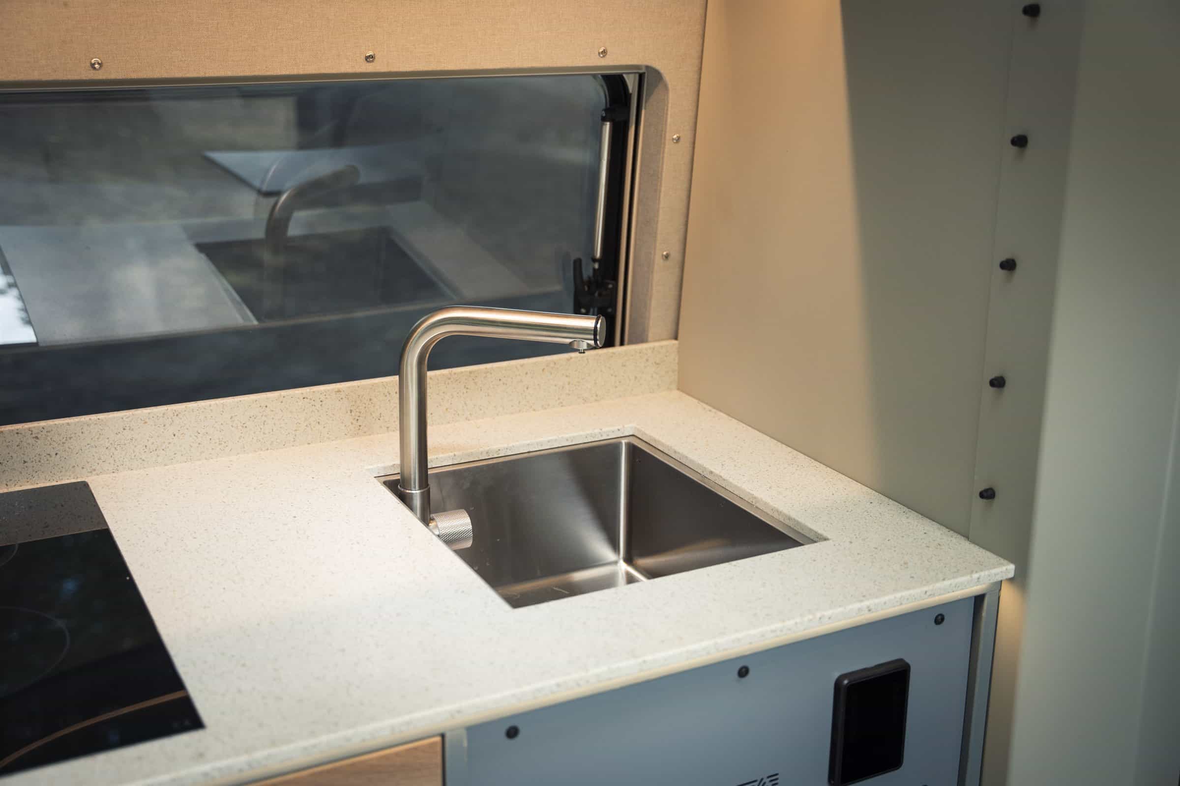 Kitchen detail in the Onyx Arête - stainless sink and tap set into the Hi-Macs worktop, induction hob alongside