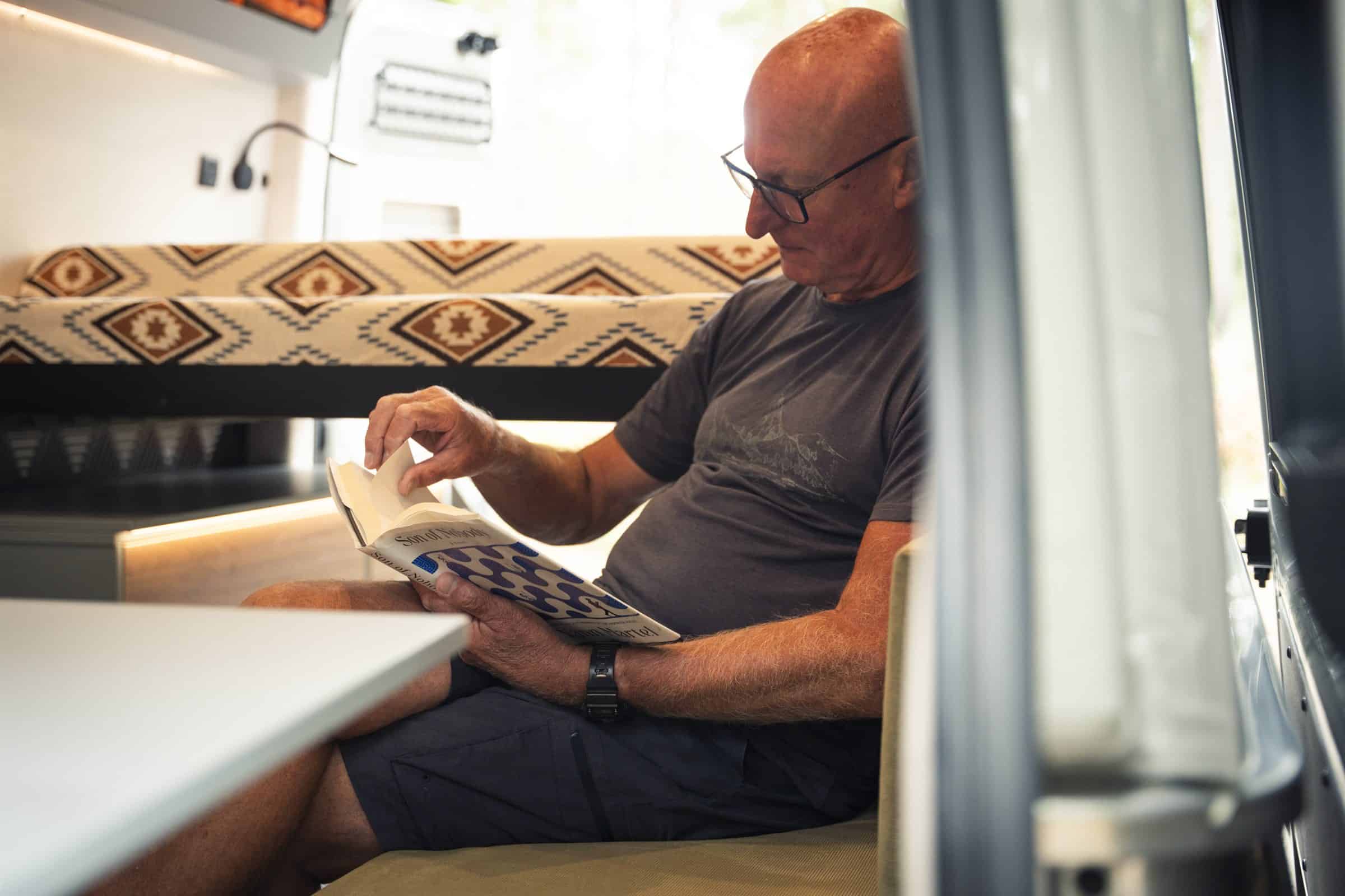 Reading on the bench seat inside the Onyx Arête, bed made up behind