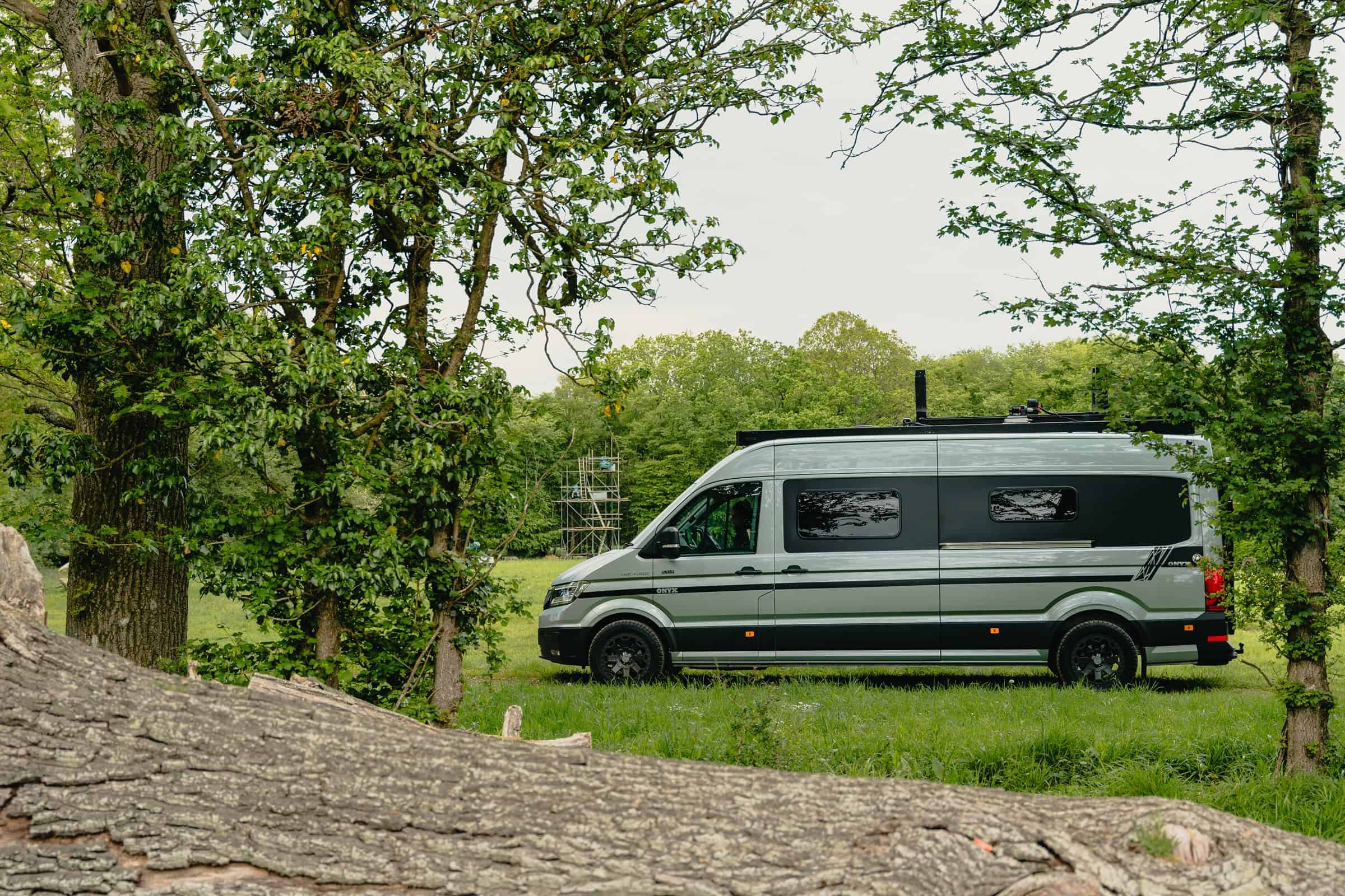 A bespoke Onyx Hors Catégorie parked among trees, with its roof rack loaded