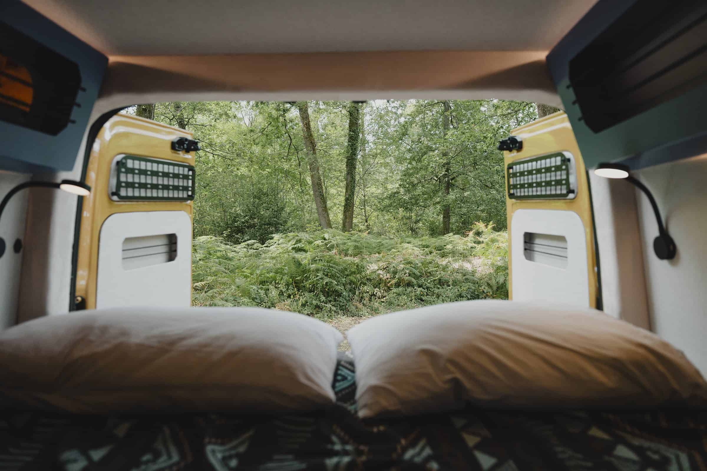 A bed made up in an Onyx campervan, looking out through the rear windows