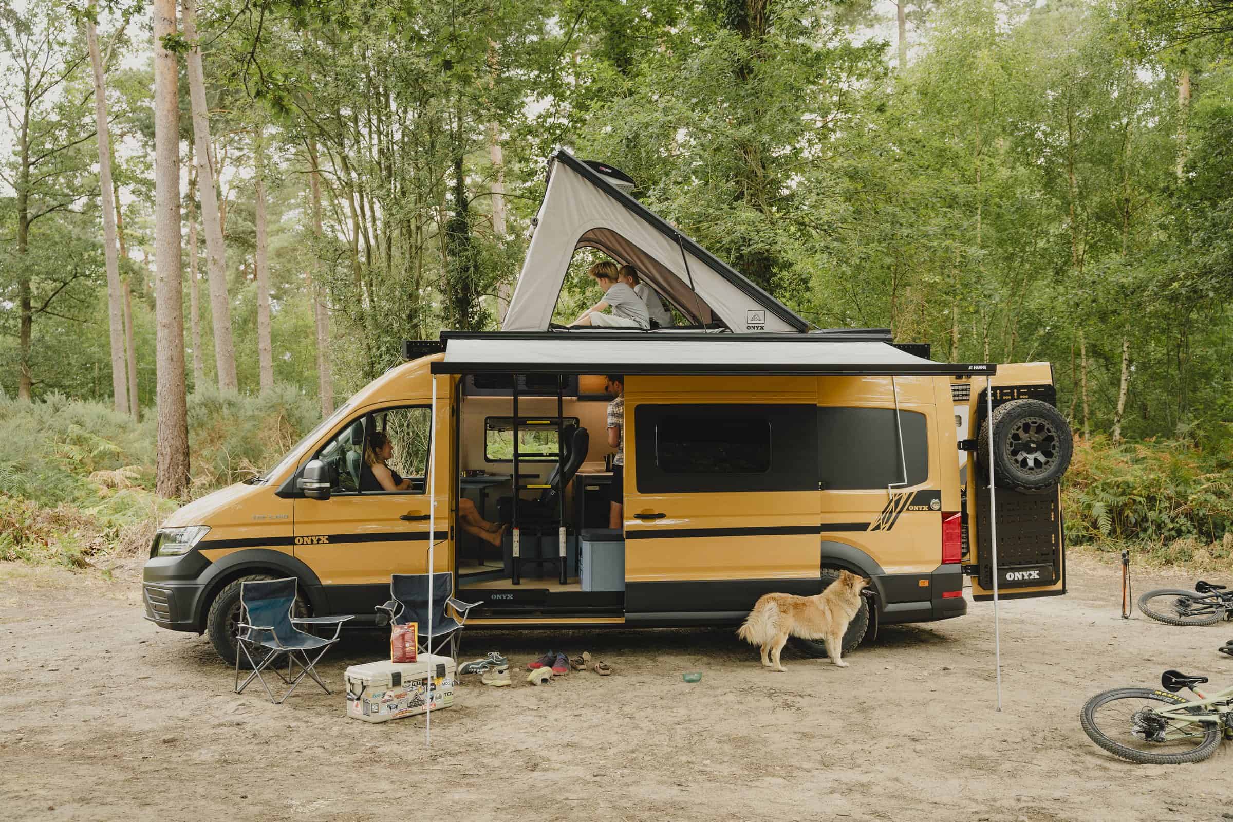 The Onyx Mesa campervan at camp in woodland, awning out and pop-top raised