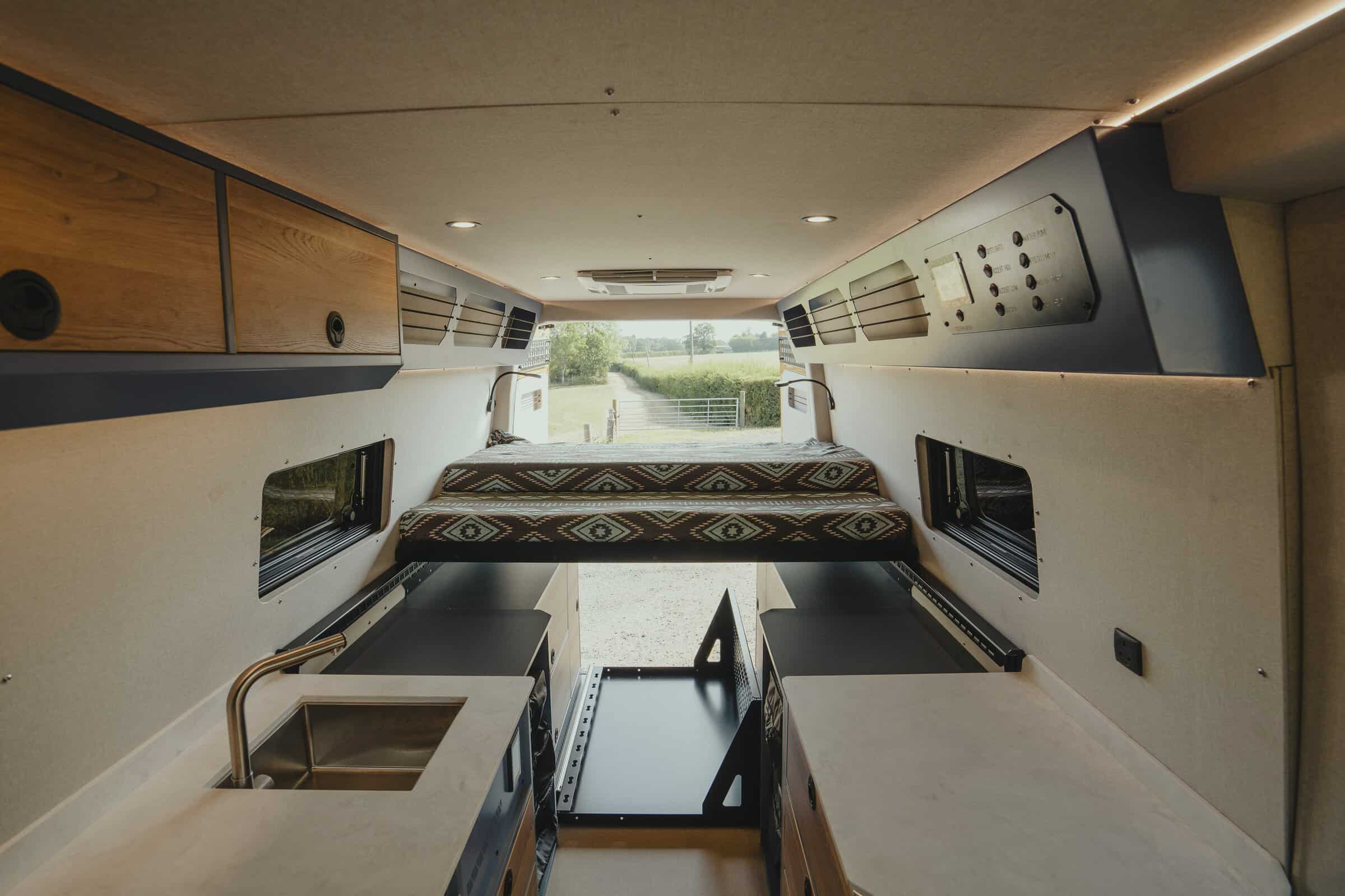 Wide interior view through the Onyx Outpost campervan to the open rear doors, galley and sliding bed