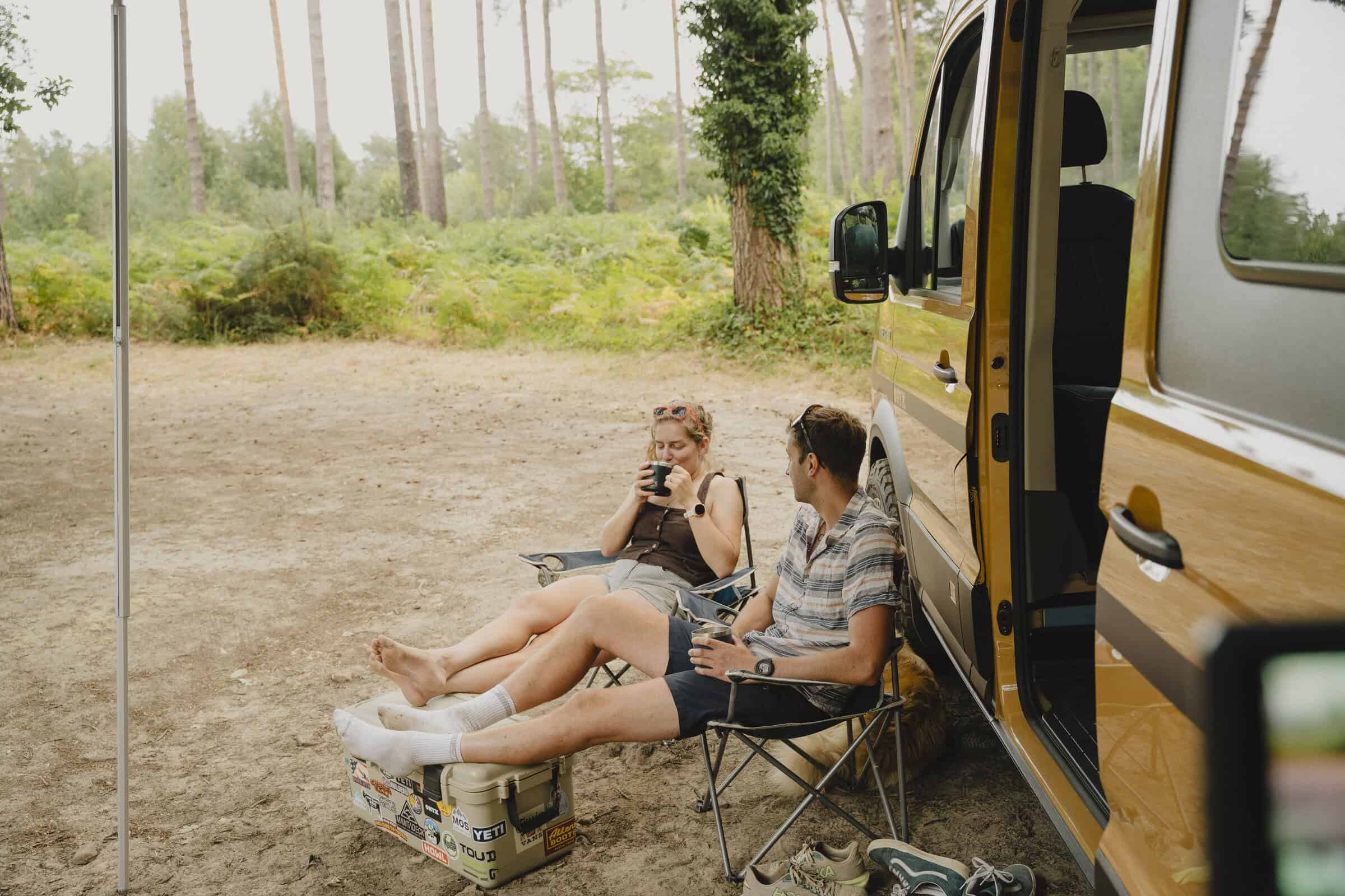 A couple relaxing in camp chairs beside the Onyx Outpost campervan