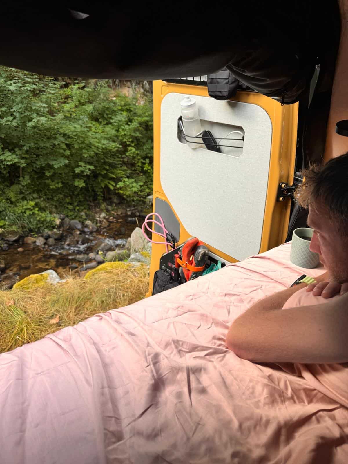 One of the boys lying in the pop-top berth, looking out through the open vent at a river and rocks