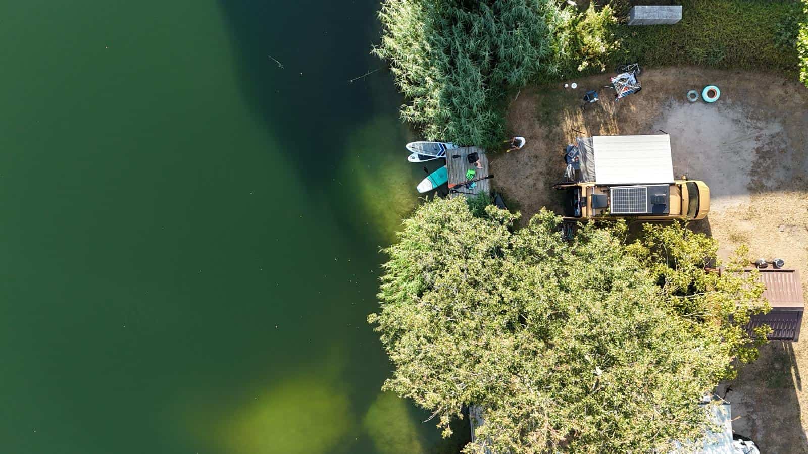 Looking straight down from above at the van parked on a lakeside pitch, with kit laid out beside the water