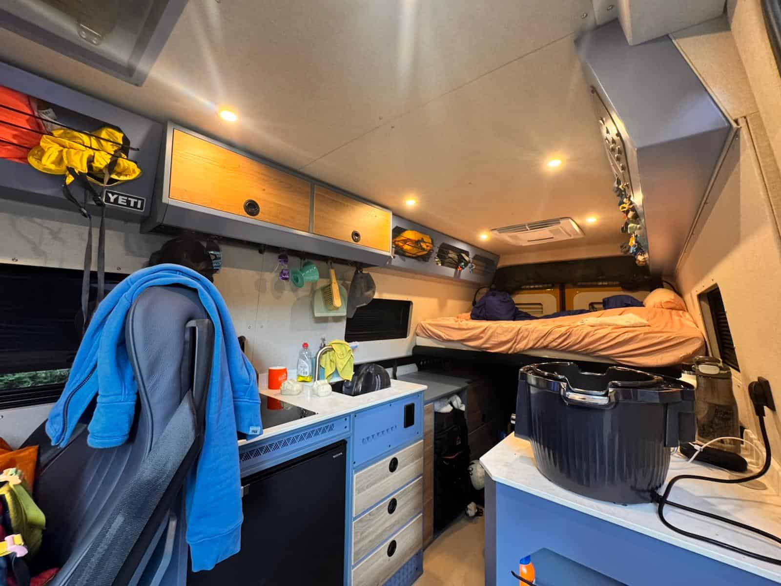 The inside of the van in use, with jackets hanging, kit in the overhead lockers and the bed made up at the far end