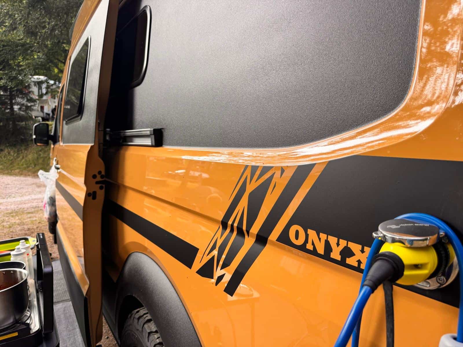 Close-up of the van's amber flank in low sun, with the Onyx chevron decal and the coiled outdoor shower hose