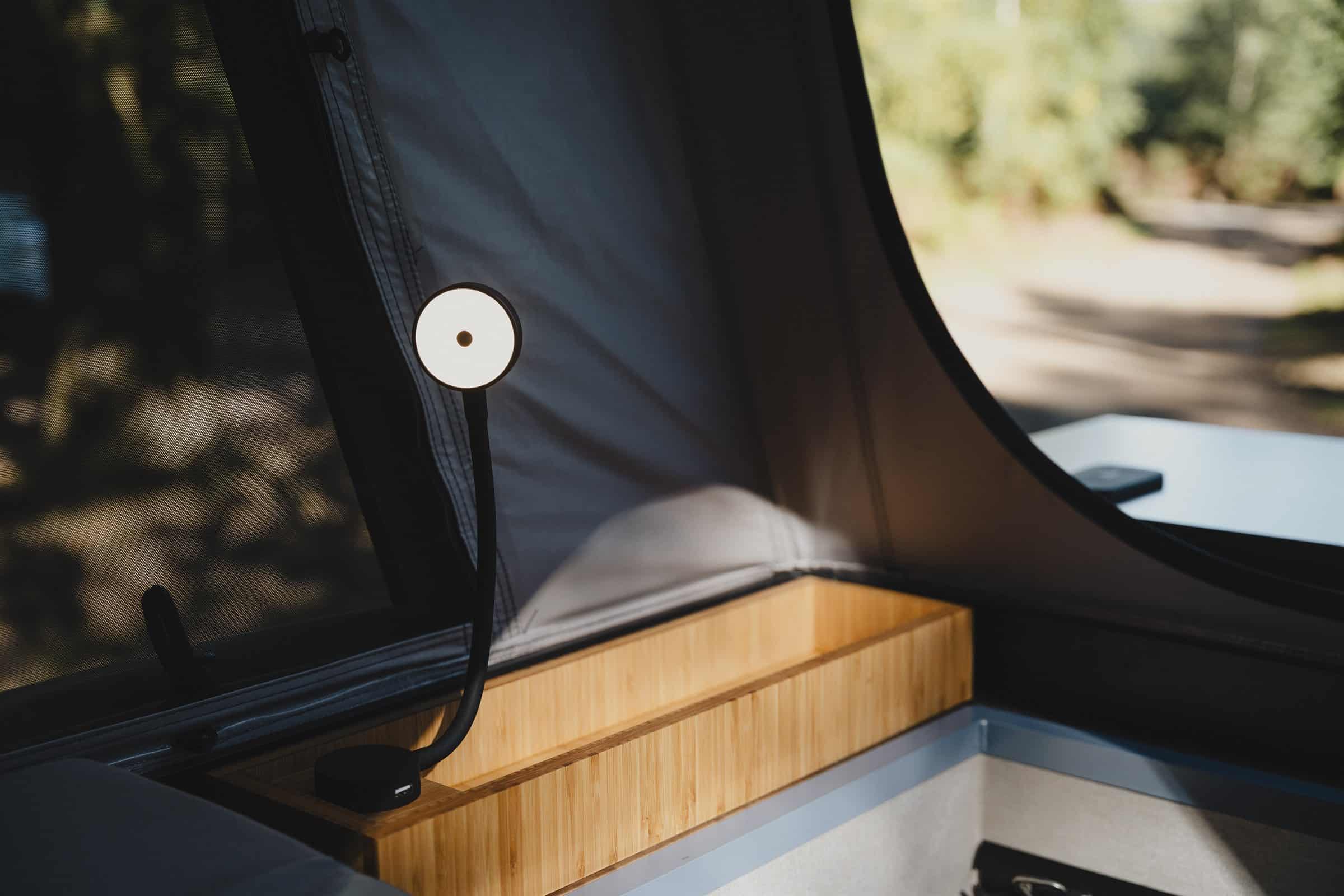 The reading light raised from a bamboo storage box inside the Onyx pop-top, with the window open behind it