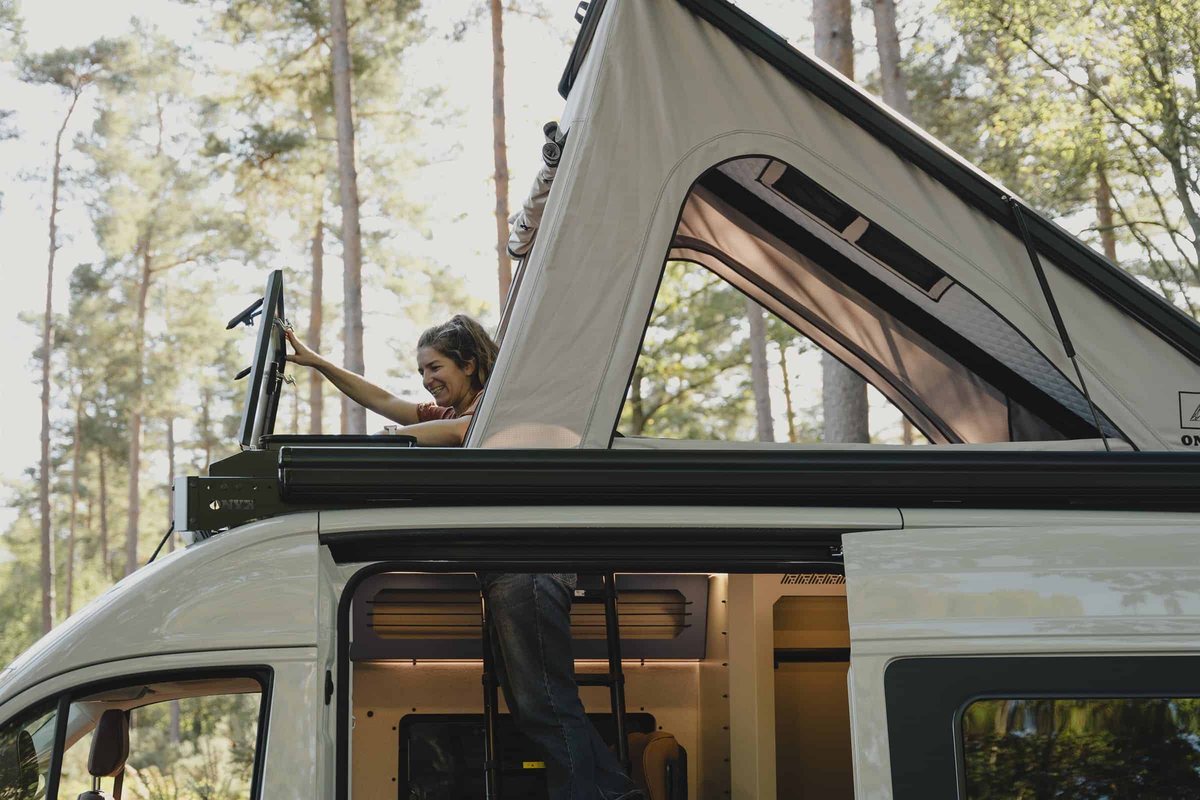 Someone leaning out of the raised Onyx pop-top to open the front storage box on the roof rack