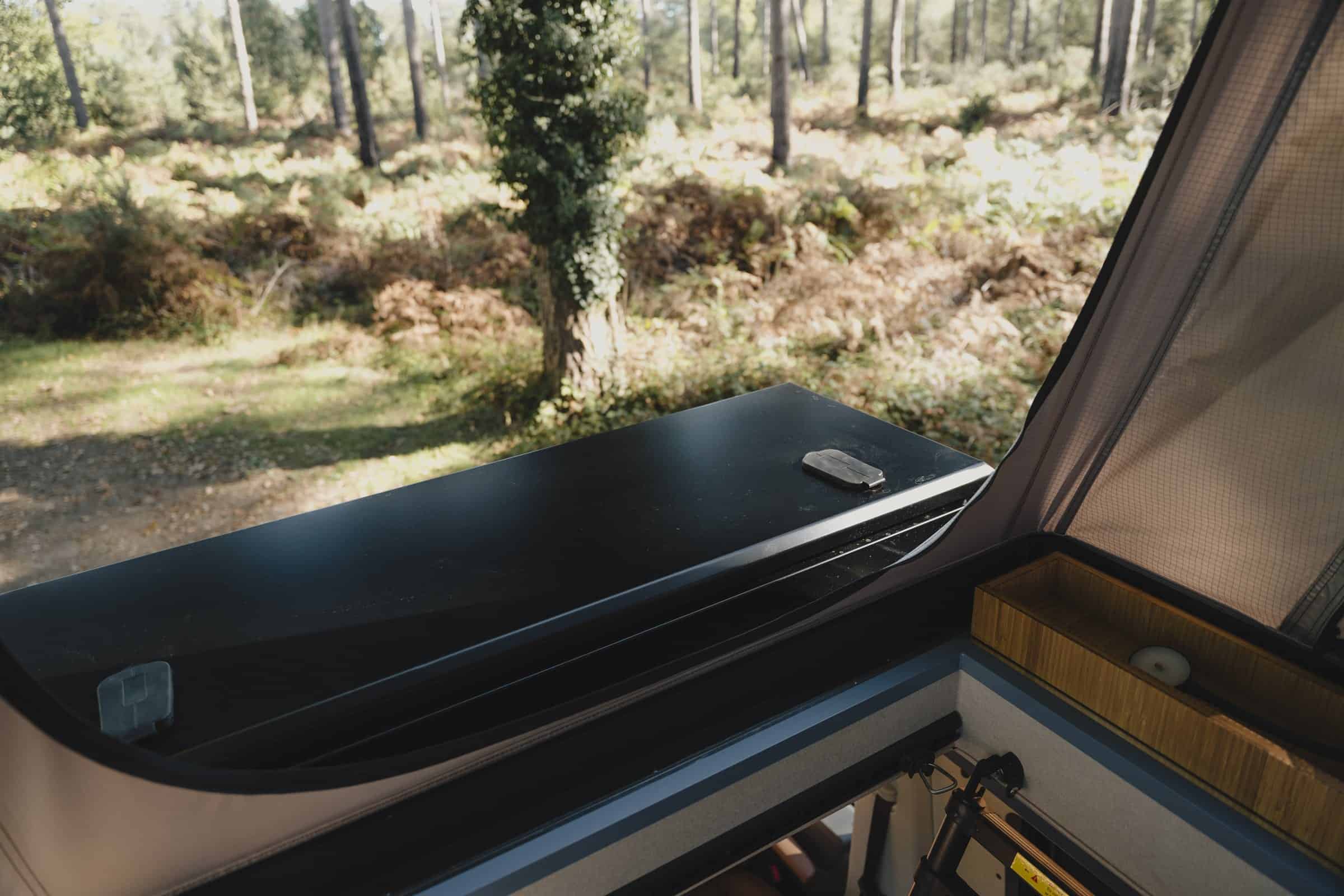 The Onyx front storage box closed on the roof rack, seen from inside the pop-top, with a bamboo storage box beside the berth