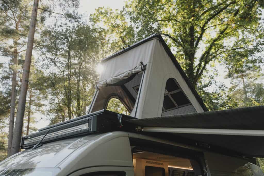 The Onyx pop-top raised on a MAN TGE in woodland, with the roof rack light bar in front of it and an awning out along the side