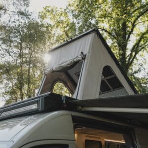 The Onyx pop-top raised on a MAN TGE in woodland, with the roof rack light bar in front of it and an awning out along the side