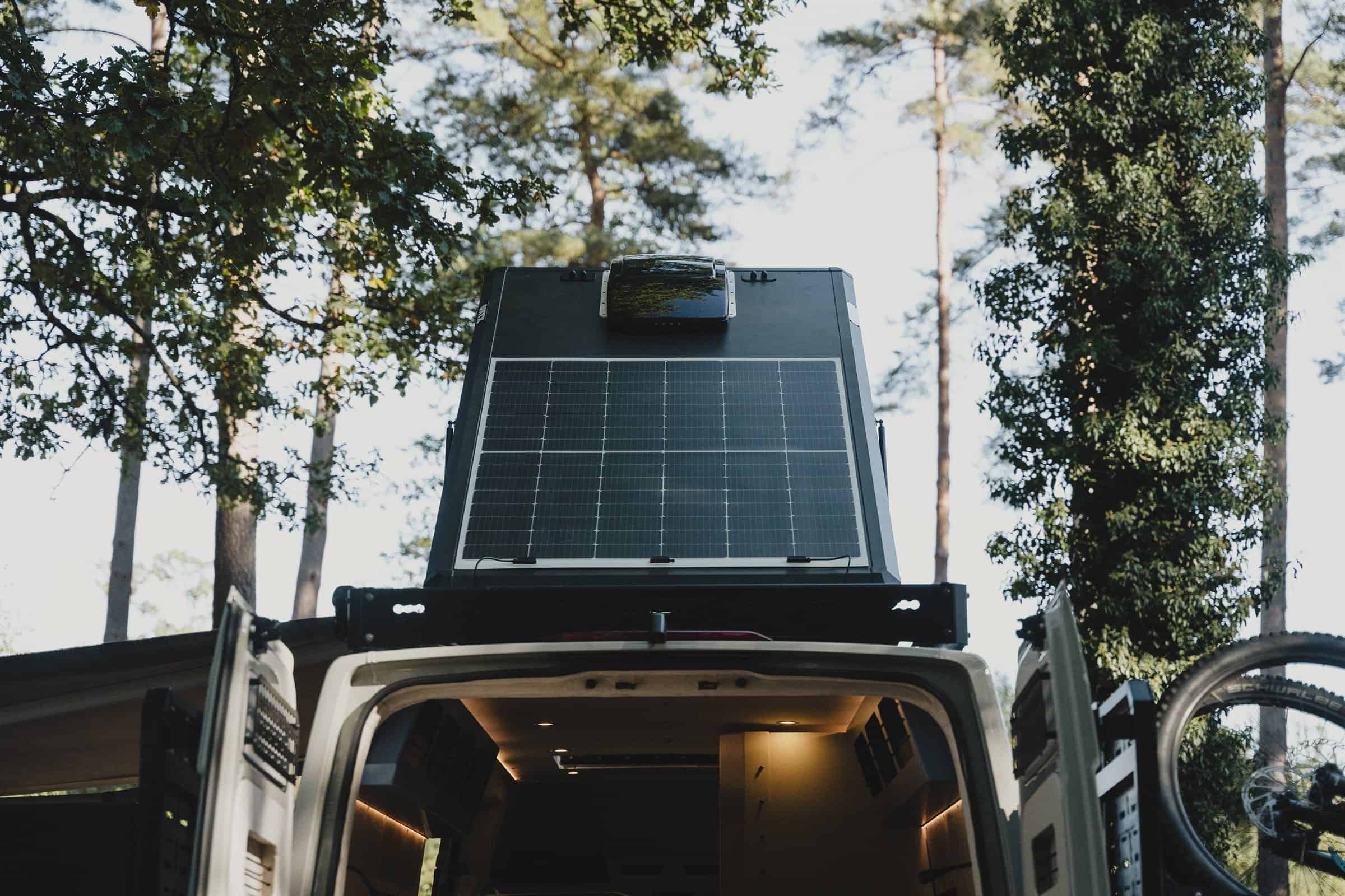 The Onyx pop-top raised, seen from behind the van, with a solar panel and a Maxxair fan on the hard shell