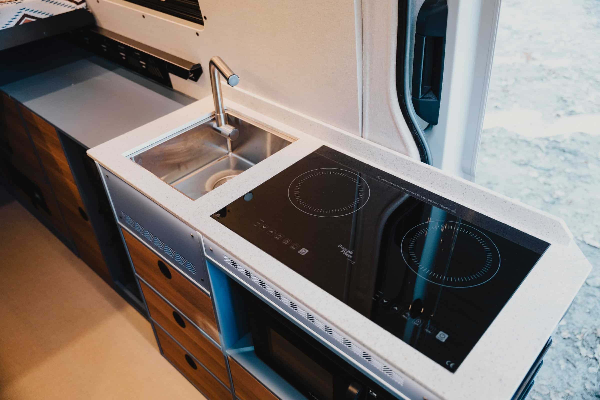 Kitchen in the Onyx Mesa with double induction hob, stainless sink and Hi-Macs worktop. Shows optional microwave