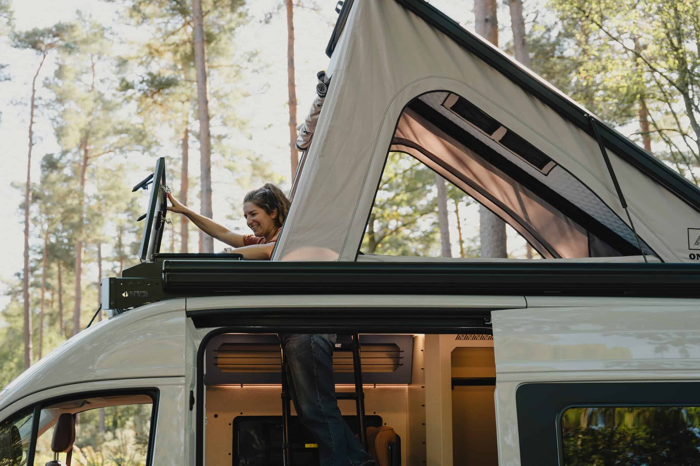 Standing on the Onyx roof rack beside the raised pop-top of the Mesa