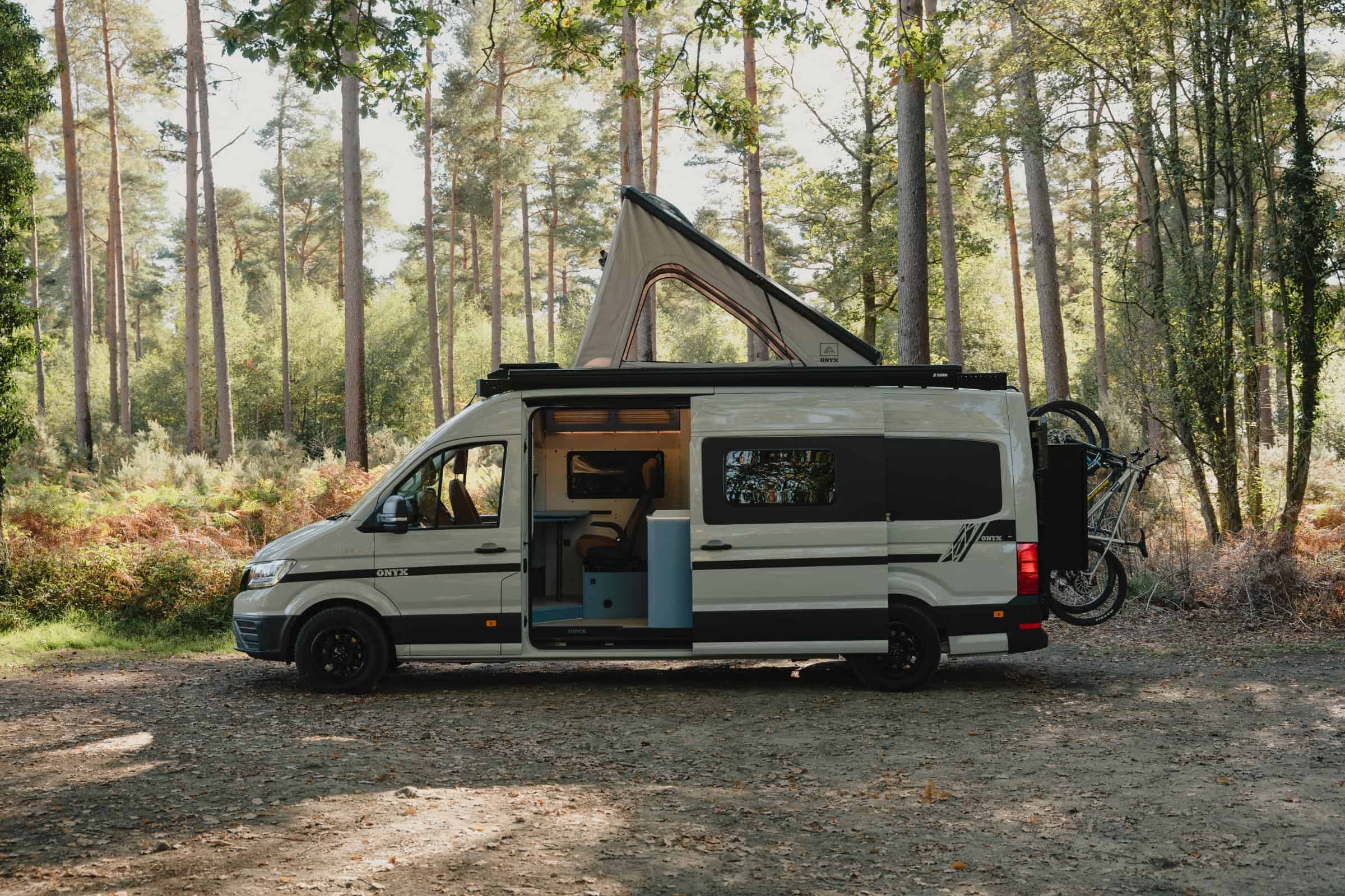 The Onyx Mesa side-on in woodland with the pop-top raised, side door open and two bikes on the rear carriers