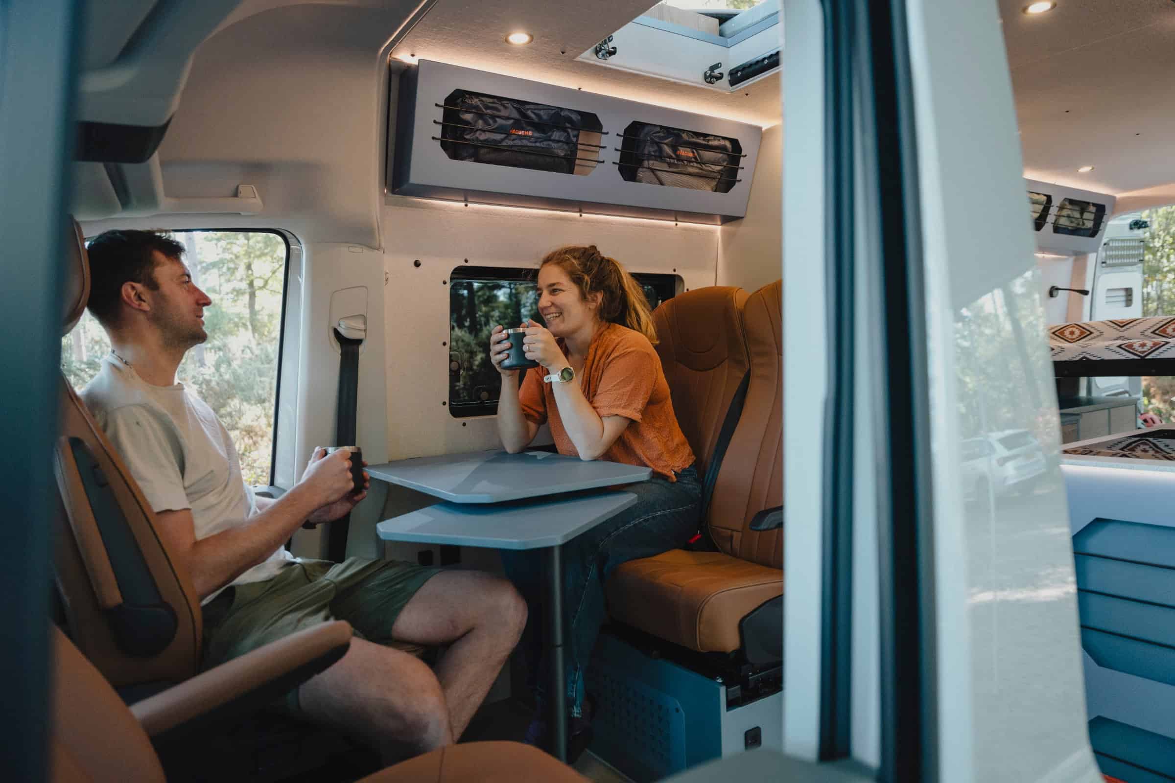 Two people with coffee at the table in the Onyx Mesa, on the belted travelling seats