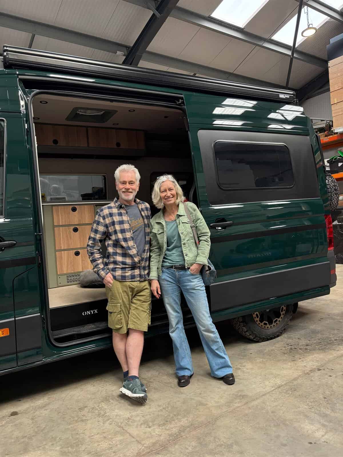 Two Onyx owners standing beside their green MAN TGE campervan in the West Sussex workshop on handover day